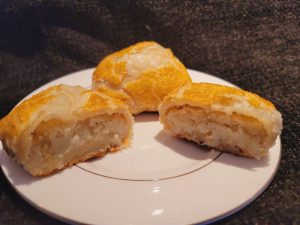 Golden-brown knishes: beef brisket cut in half, revealing its flaky interior, on a white plate.