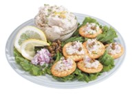 A plate of chopped herring topped with a spread, accompanied by a side of mashed potato and lemon wedges, garnished with lettuce leaves.