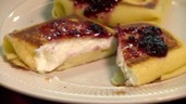 Two blintzes with cheese filling and berry sauce on a plate.