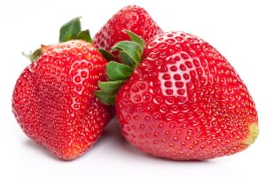 A close up of three strawberries on a white surface