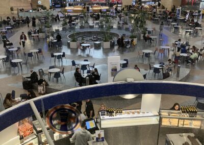 A bustling airport food court with travelers dining and walking about.