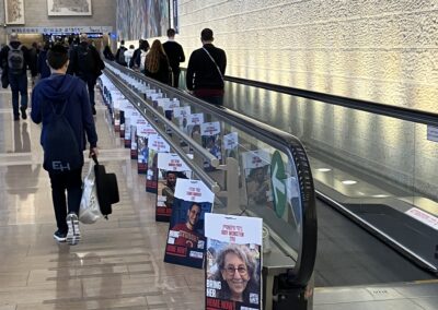People walking beside a moving walkway lined with posters on the floor.