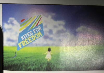 A child standing in a field with a colorful kite graphic and the words "kites for freedom" displayed above.