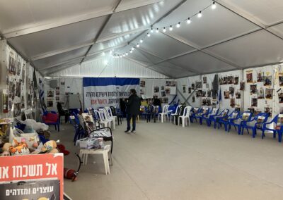 Temporary memorial space with chairs, photographs, and israeli flags inside a tent.