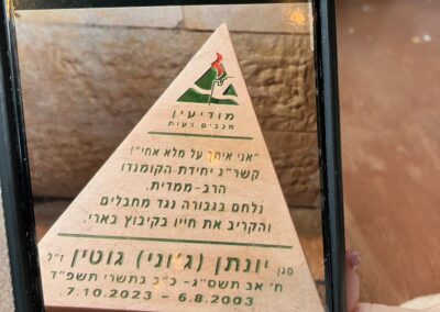 A person's hand holding a smartphone displaying a photo of a triangular sign with hebrew text and a camel graphic, symbolizing caution in a desert area.