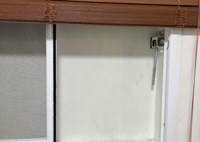 Window with brown blinds partially raised, showing a frosted glass for privacy.