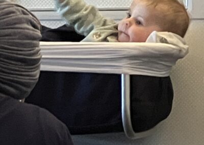 A baby reclining in an airplane bassinet, looking relaxed and observing their surroundings.