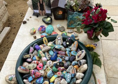 A collection of painted stones placed as memorials on a grave.